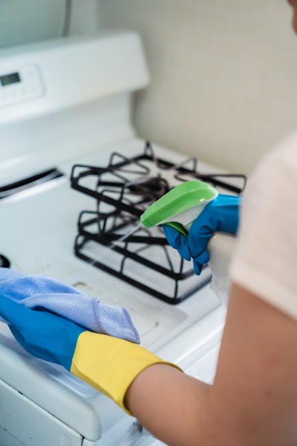 Three professional cleaners from Cleaners Richmond are engaged in surface cleaning within a modern living room, featuring a light-colored tiled floor, a grey fabric sofa, and large windows allowing na